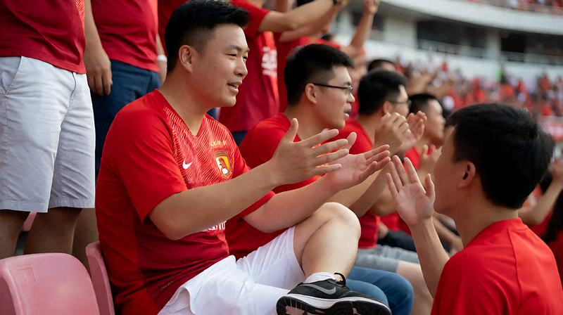 足球场看台上的球迷挥舞围巾为球队助威，现场气氛热烈